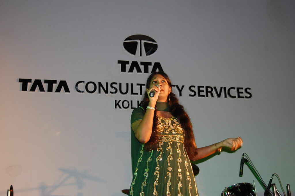 Mouli Chakrabarti singing on stage in front of the Tata Consultancy Services sign in Kolkata.