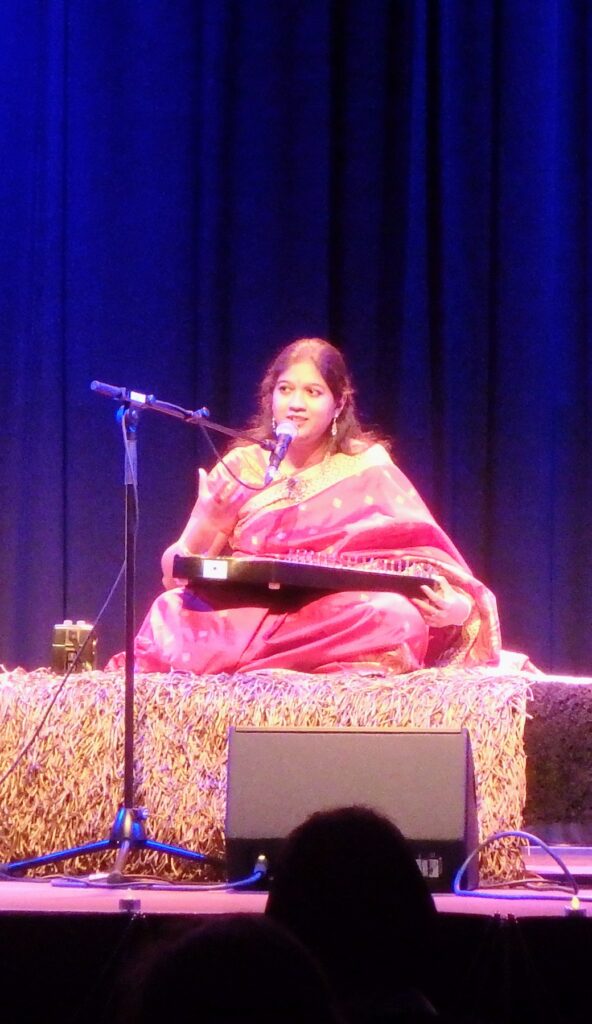 Mouli Chakrabarti performing seated with a microphone and lap instrument at a concert in Mainz.